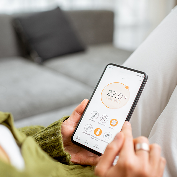 Imagen mostrando a una persona sujetando un smartphone mientras configura la temperatura de su casa mediante una app